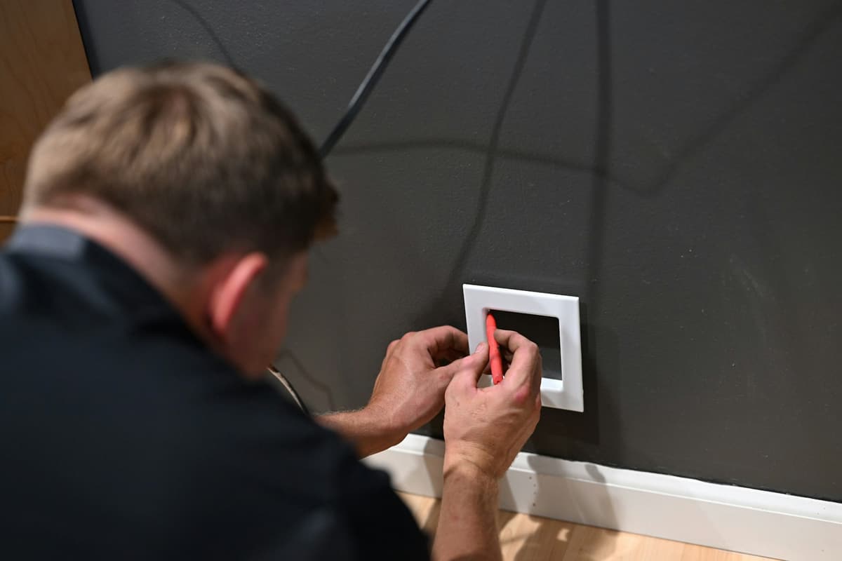 Monteur setzt einen Schalterrahmen an einer grauen Wand