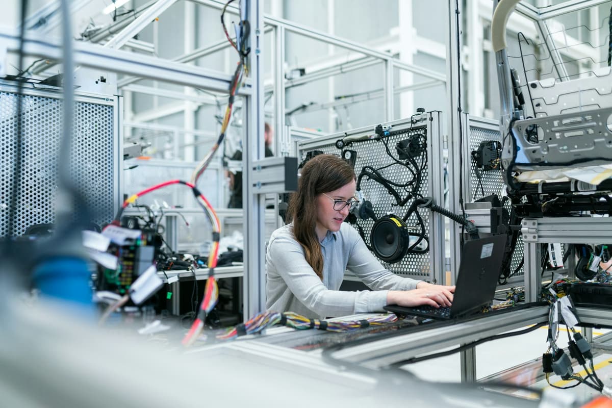 Ingenieurin arbeitet am Laptop an einem Prüfstand mit Kabelbäumen und Fahrzeugkomponenten