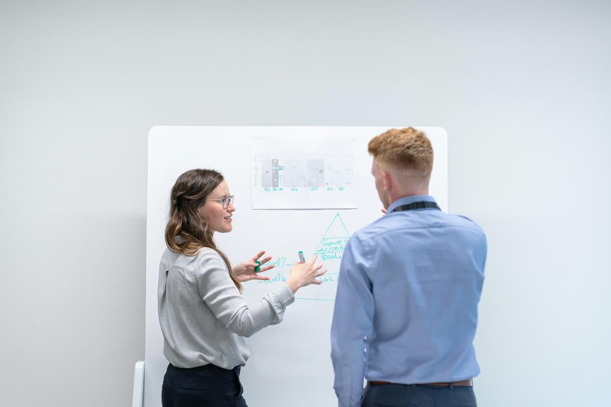 Zwei Kollegen besprechen einen ausgedruckten Ablaufplan am Whiteboard