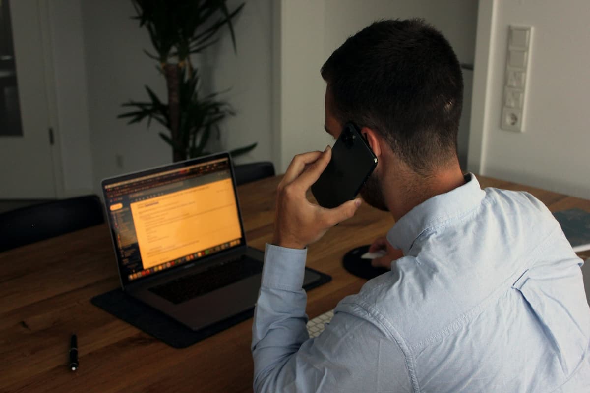 Mann telefoniert am Schreibtisch neben dem aufgeklappten Laptop
