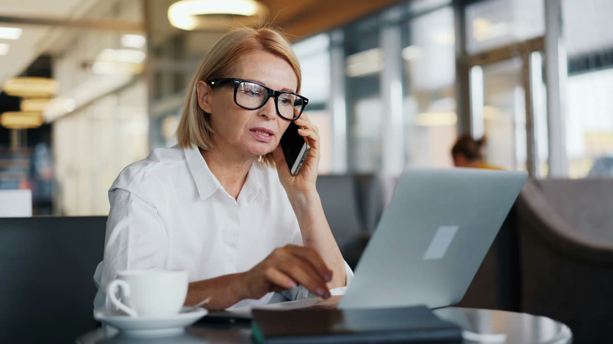 Frau mit Brille telefoniert konzentriert und arbeitet dabei am Laptop
